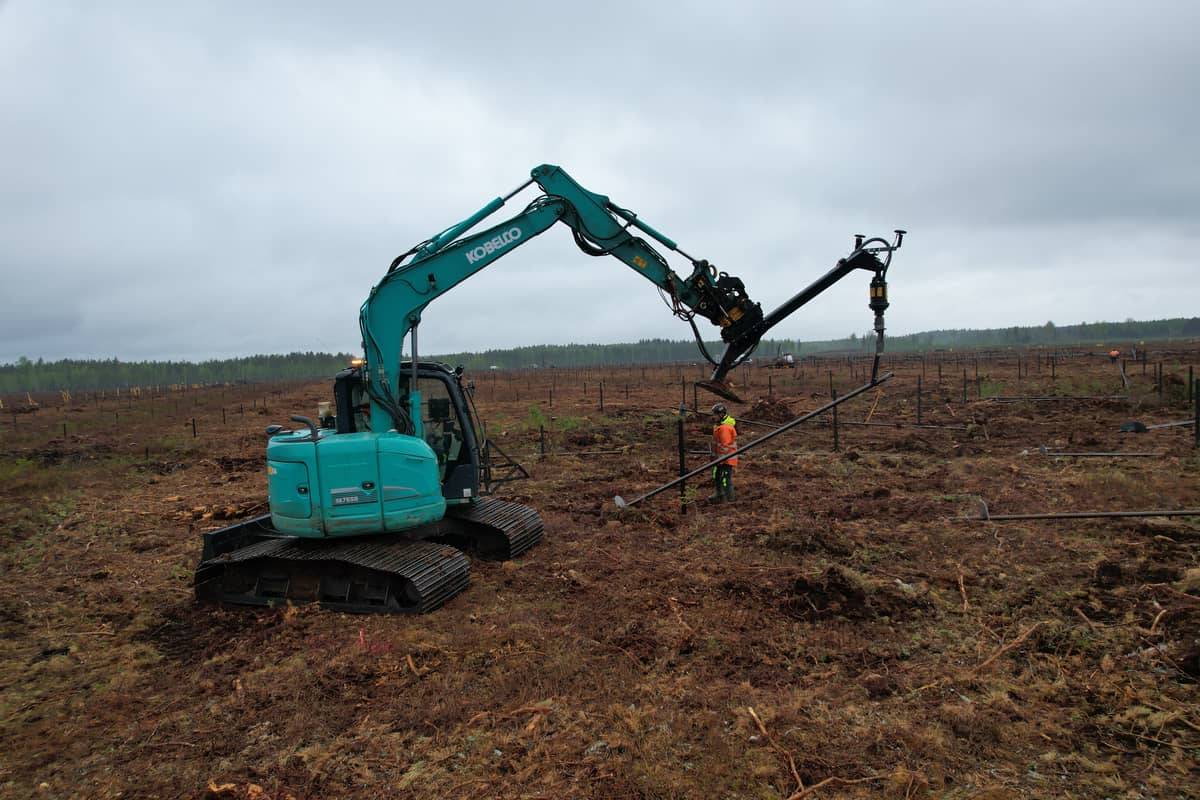 Kobelco rig and operator pulling a helical pile, overcast day at Hallanvahti
