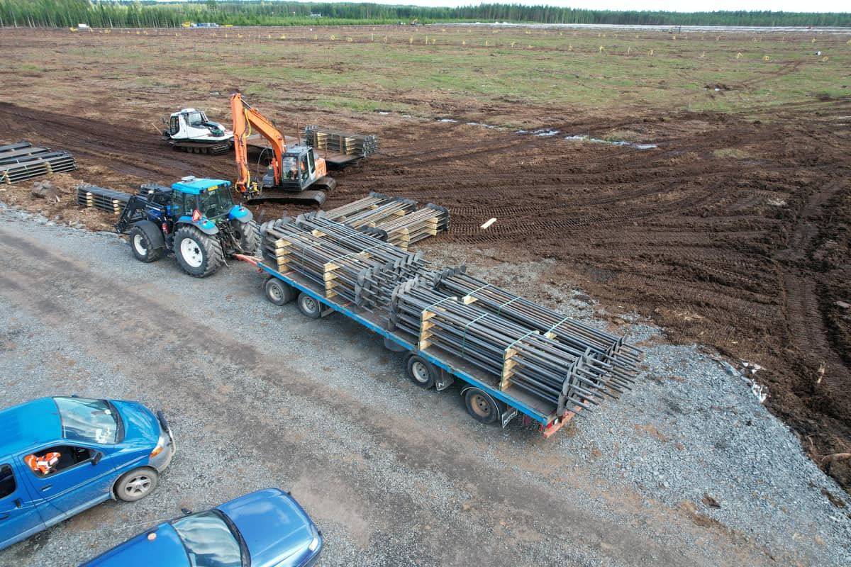 Pile delivery on site: tractor-trailer of bundled helical piles, Kobelco rig in background