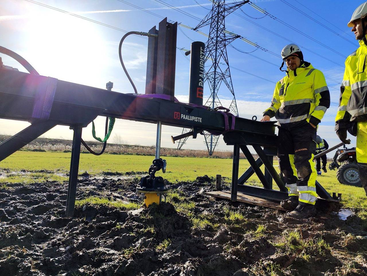Helicasolin asennusryhmä työmaalla pohjoismaisessa aurinkohankkeessa — ruuvipaalua kierretään voimajohdon alla talvella